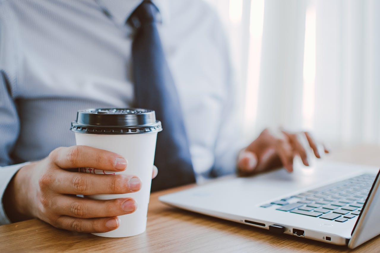 hero Business professional working remotely, enjoying coffee while using a laptop indoors.